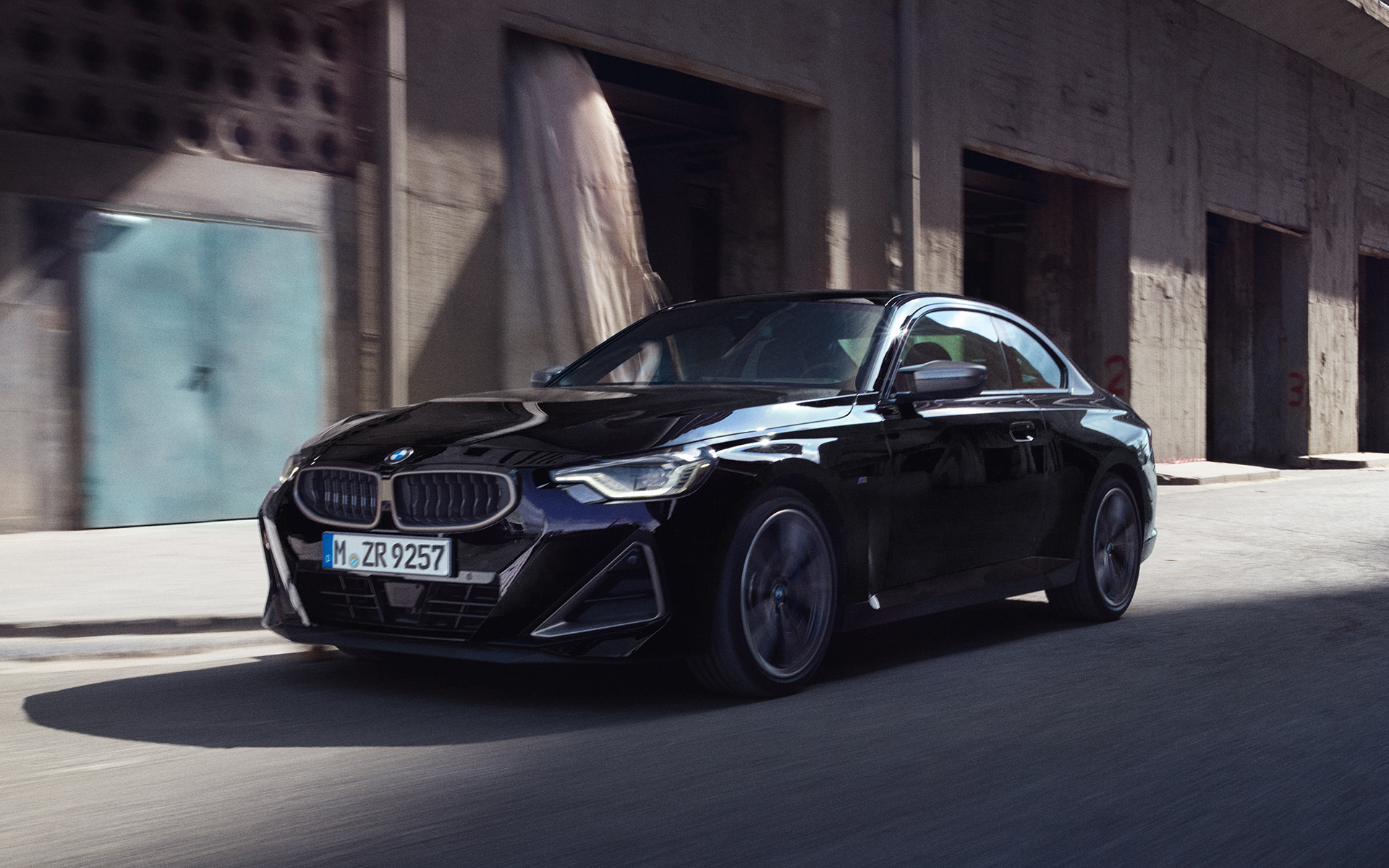 G42 BMW M240i xDrive雙門跑車Black Sapphire銀粉漆，行駛於倉庫前，四分之三車頭視角