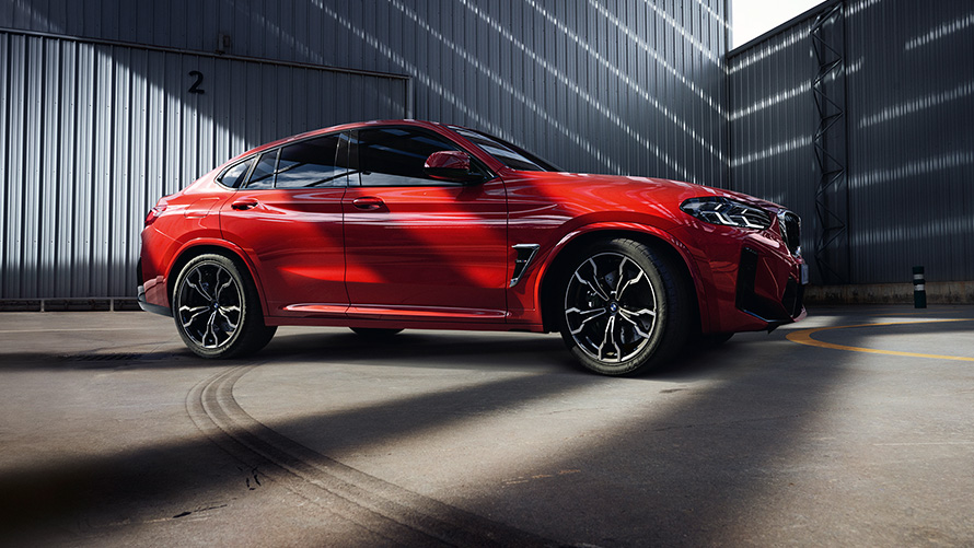F98 BMW X4 M LCI嶄新風貌，Toronto Red銀粉漆，於工廠建築物前，車側視角