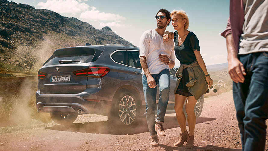 F48 BMW X1 LCI,Storm Bay,四分車三車尾視角 F48 BMW X1 LCI,Storm Bay,靜止,於景色前方,且有人們位於其前方,四分車三車尾視角