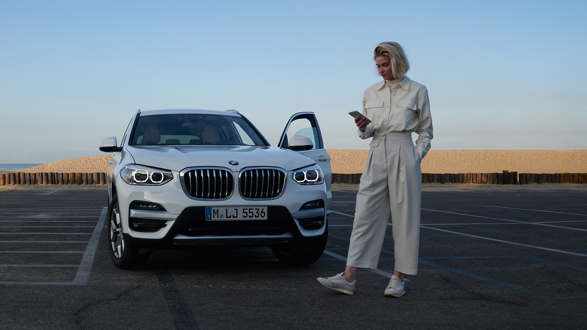 女性使用智慧型手機享受My BMW App服務 女性在白色BMW X5前使用智慧型手機享受My BMW App服務