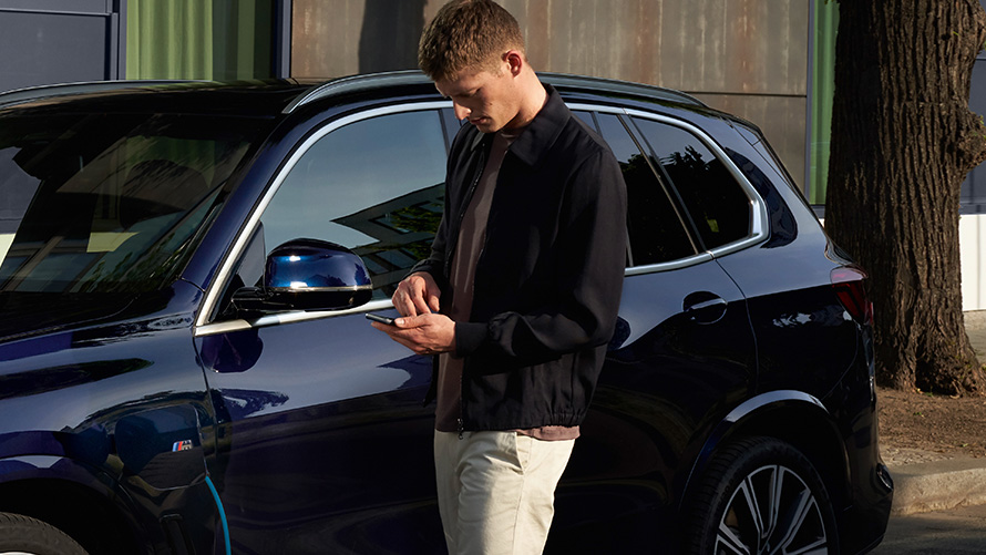 遠端軟體升級，男人於BMW前方注視著他的智慧型手機